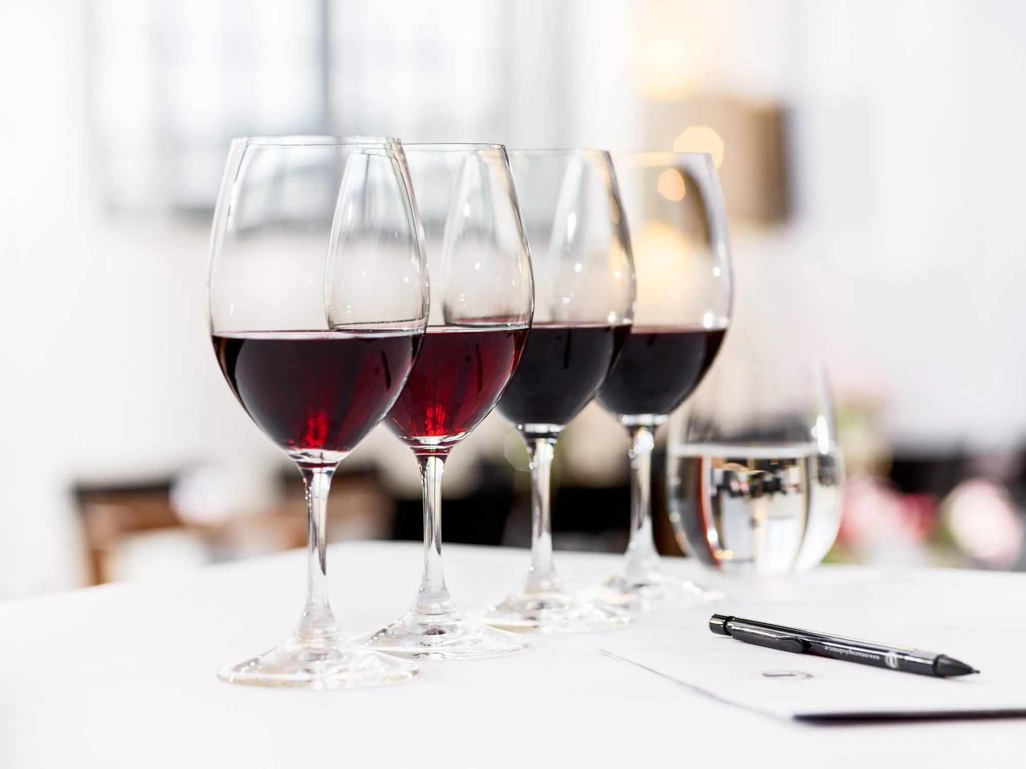Fyra vinglas på rad fyllda med rött vin av olika nyanser