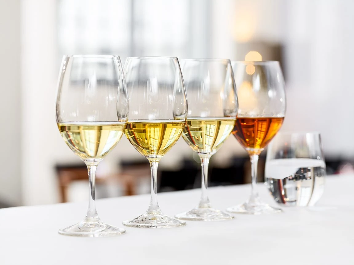 Fyra vinglas på rad fyllda med vitt vin av olika sorter