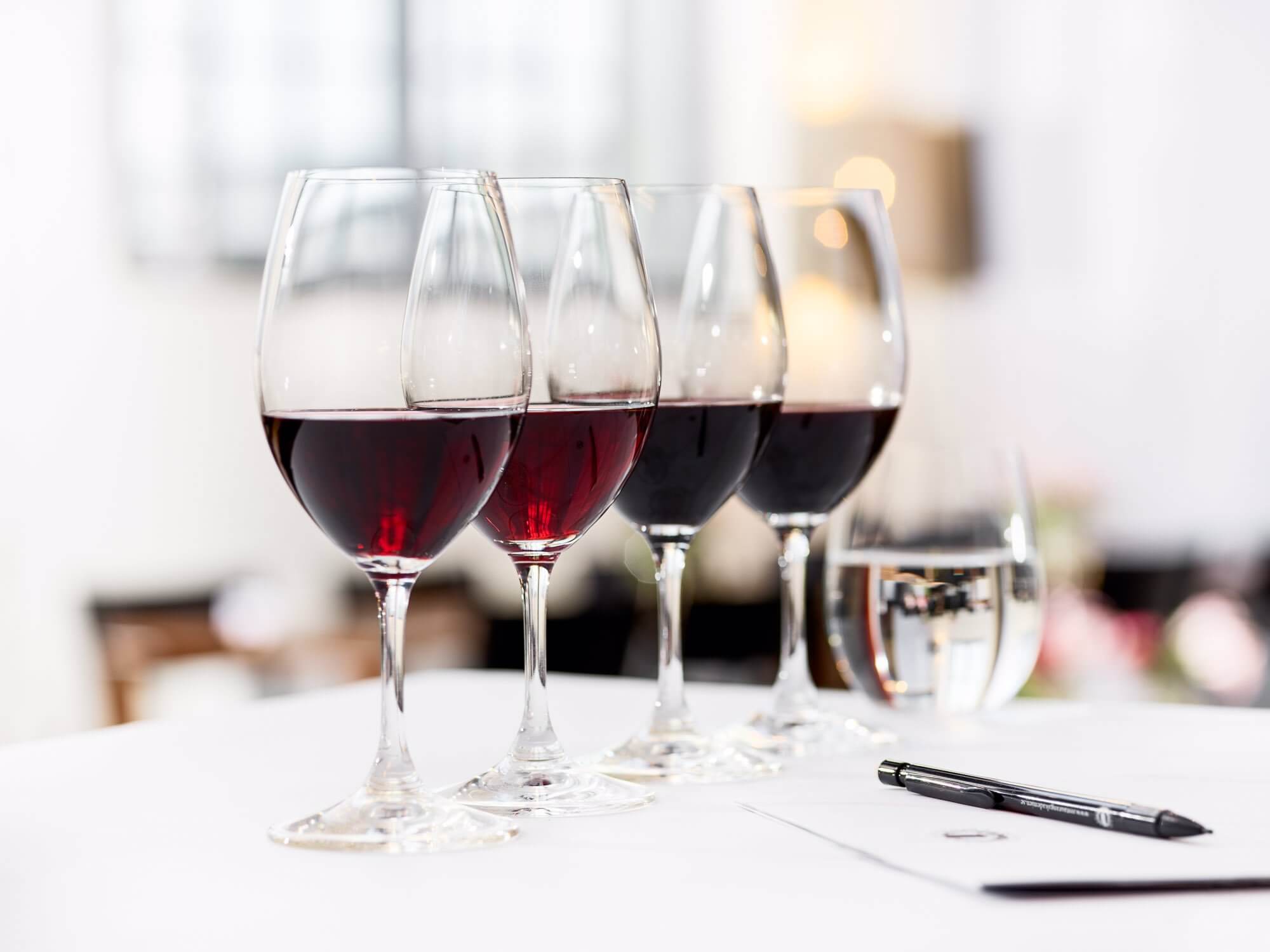 Fyra vinglas på rad fyllda med rött vin av olika nyanser